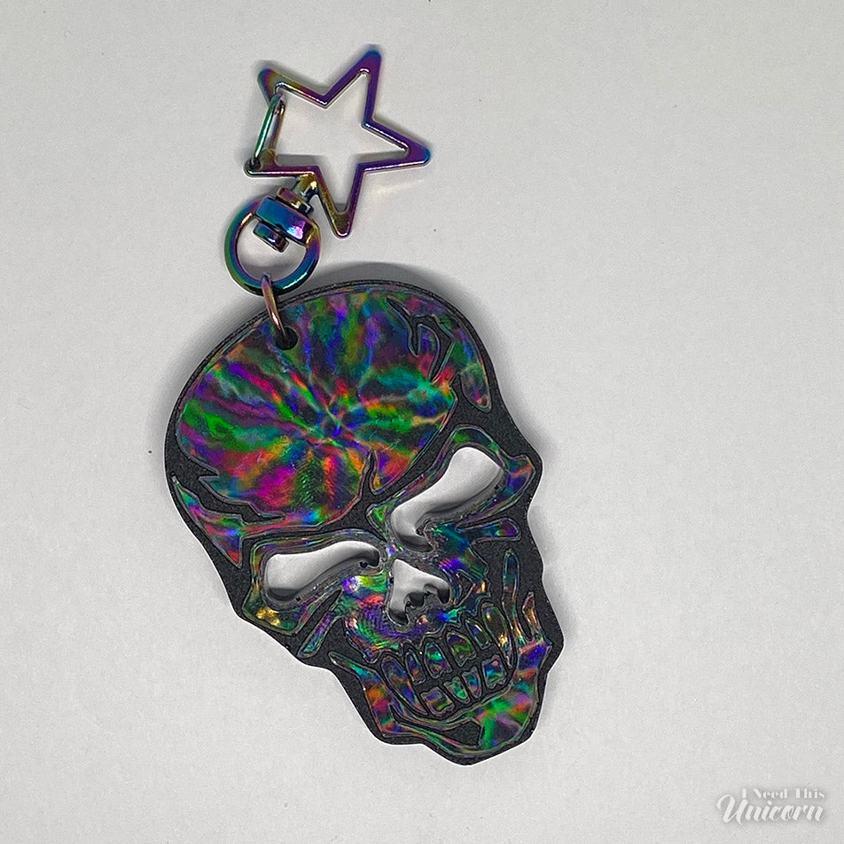 Black skull keychain with a holographic sheen and a rainbow oil-slick star clasp