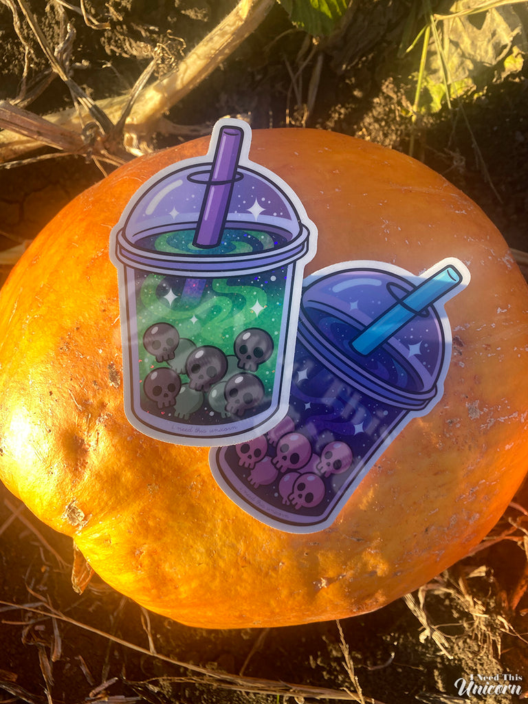 Pair of holographic boba stickers — Galactic Haunted Boba and Witch’s Brew Boba — featuring space and witchy drink designs with skull pearls on top of a pumpkin in a pumpkin patch