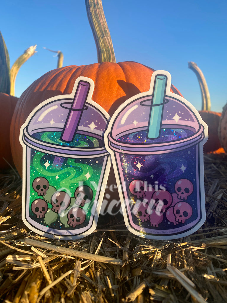 Side-by-side image of the Witch’s Brew Boba and Galactic Haunted Boba stickers. The Witch’s Brew glows in green holographic hues while the Galactic version sparkles in cosmic purple and blue. Both shimmer under natural sunlight.
