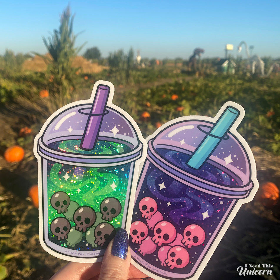 Holographic Galactic Haunted Boba & Witches Brew Boba stickers held in hand to show large 3.5 by 5 inch size and reflective finish.