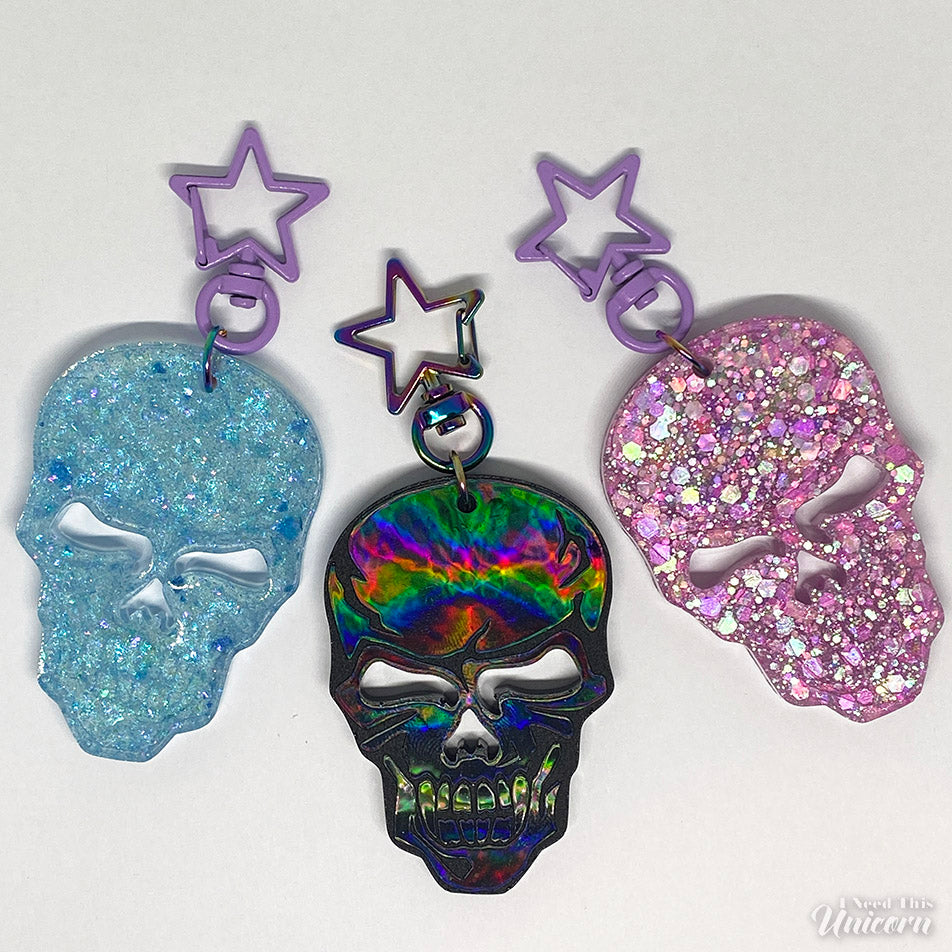 Blue glitter, black skull  and pink glitter keychains with a holographic sheen and a rainbow oil-slick star clasp