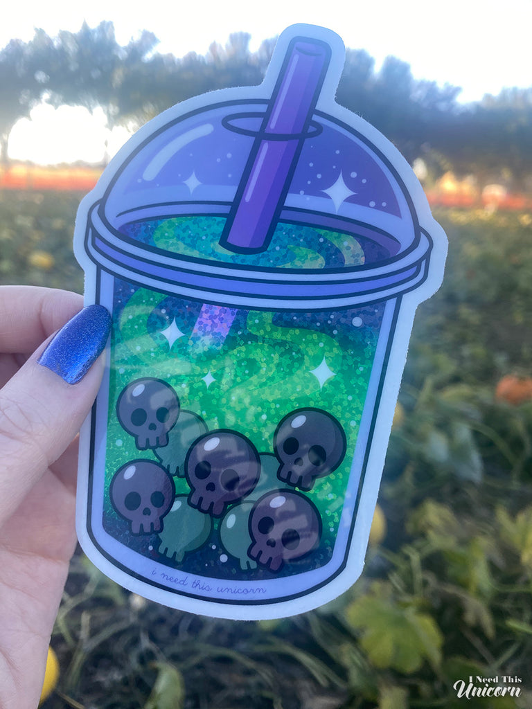 Witch’s Brew Boba Sticker photographed at a pumpkin patch. The sticker features glowing green holographic swirls and skull-shaped boba pearls inside a spooky bubble tea cup. Accented holographic finish, as shown in the shade.