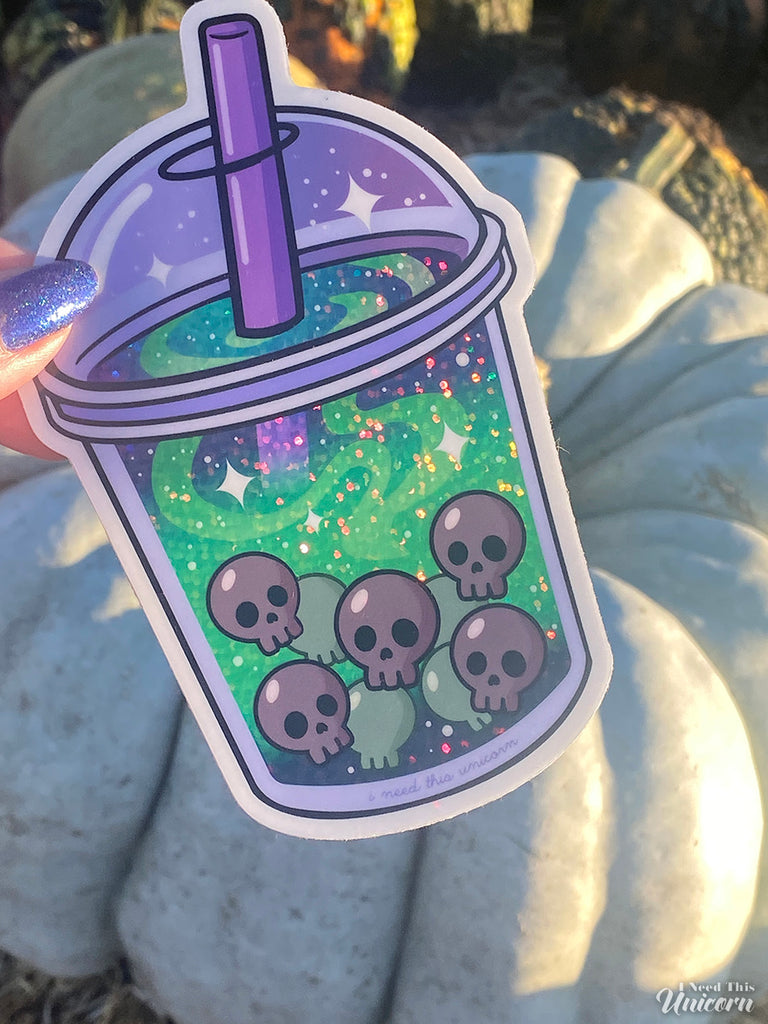 Witch’s Brew Boba Sticker photographed at a pumpkin patch. The sticker features glowing green holographic swirls and skull-shaped boba pearls inside a spooky bubble tea cup. Accented holographic finish catches the light. Pictured in a pumpkin patch on a white pumpkin.